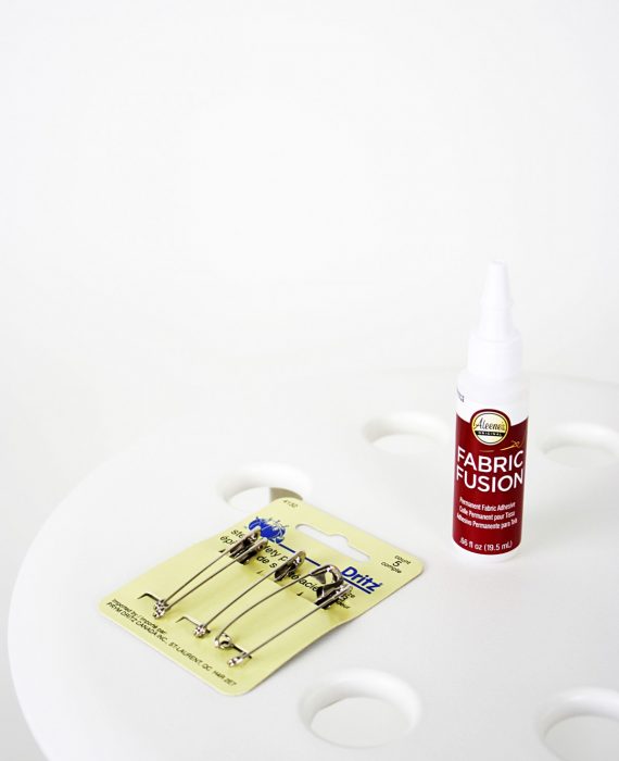 Materials for DIY fuzzy stool: fabric glue and safety pins pictured on top of stool