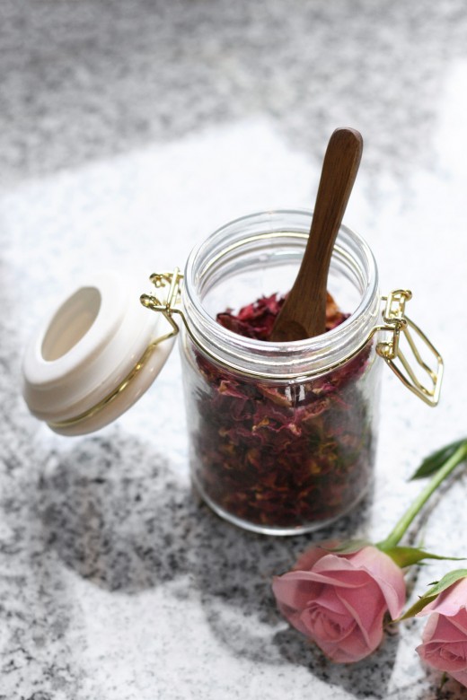 Small glass jar of organic dried rose petals with wooden spoon