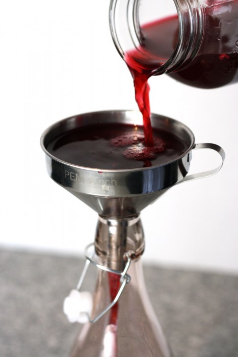 Straining the rose petal vinegar into a glass bottle with steel funnel