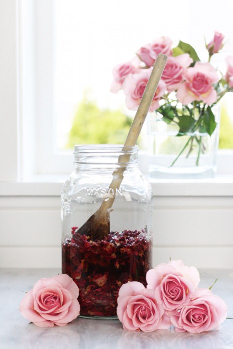 Wooden spoon pushing rose petals into glass jar