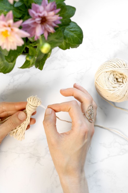 Threading cotton string through handmade cotton tassel for wood garland