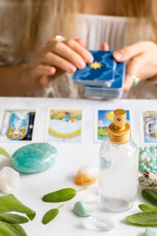 Cleansing Tarot cards with aura spray. Woman Tarot reading with crystals and sage.