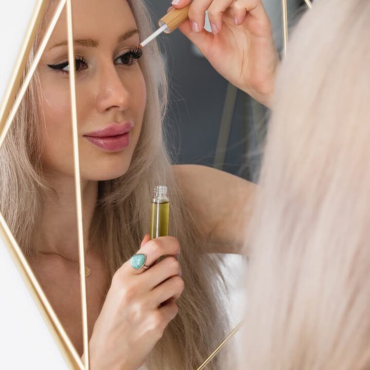 Woman applying DIY eyelash growth serum in mirror
