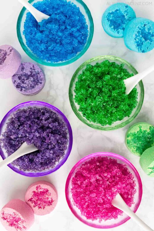 Bowls of colored Epsom salts glitter in pink, purple, blue and green.