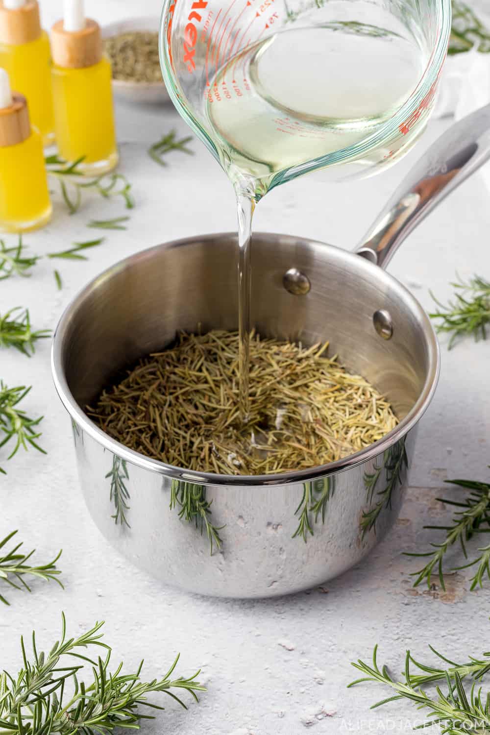Pouring castor oil and coconut oil into pot of dried rosemary.