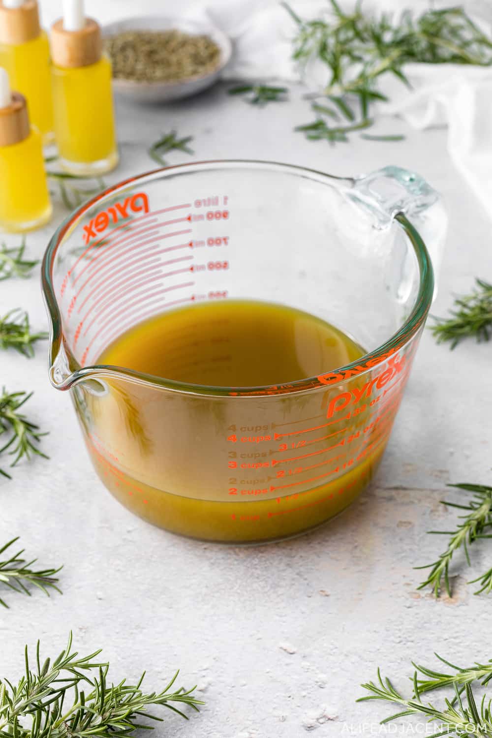 Strained rosemary oil in glass Pyrex cup.