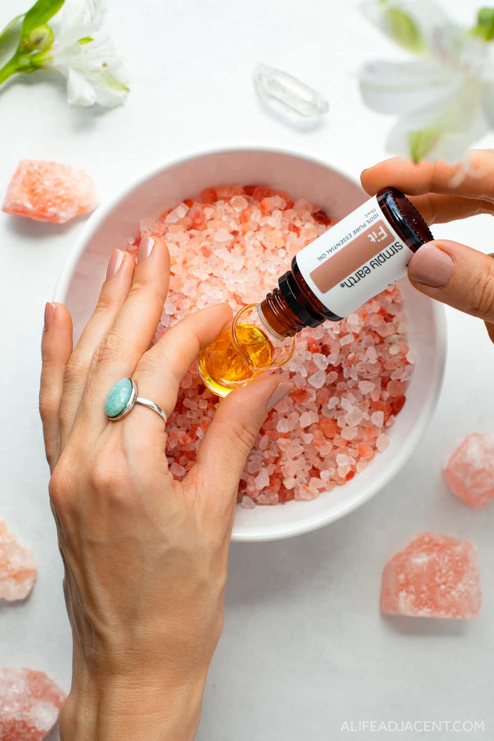 Pouring essential oils for Himalayan salt bath benefits into glass beaker