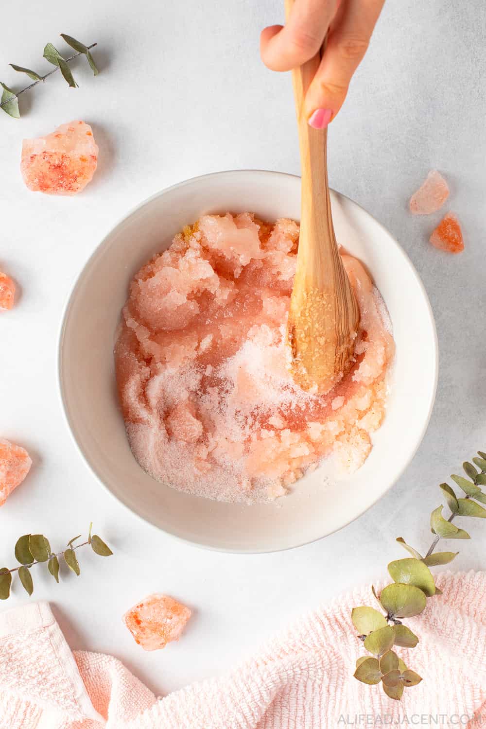 Mixing DIY pink salt scrub with wooden spoon.