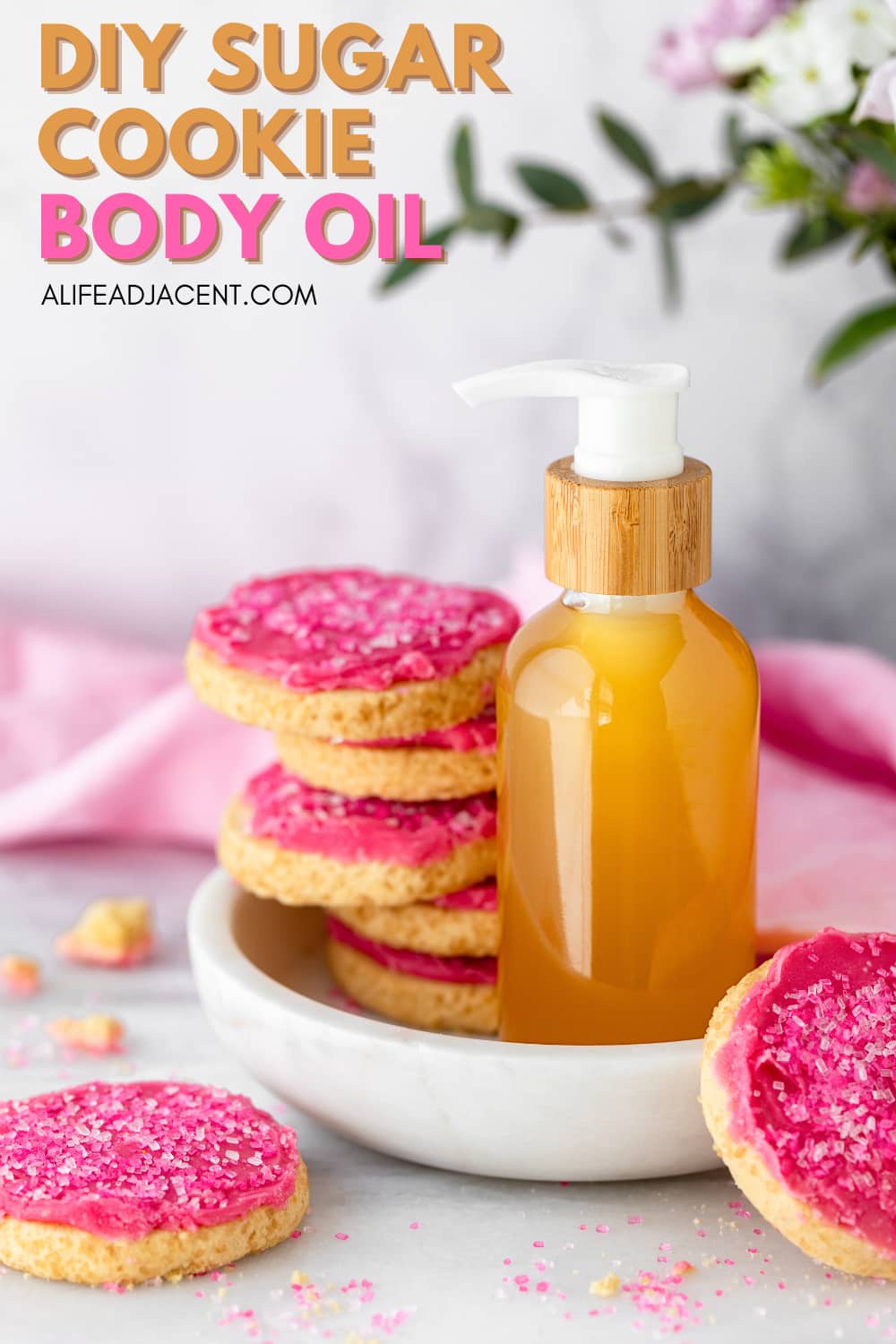 Pinterest graphic for a DIY sugar cookie body oil recipe featuring a bottle of homemade body oil and pink frosted sugar cookies.