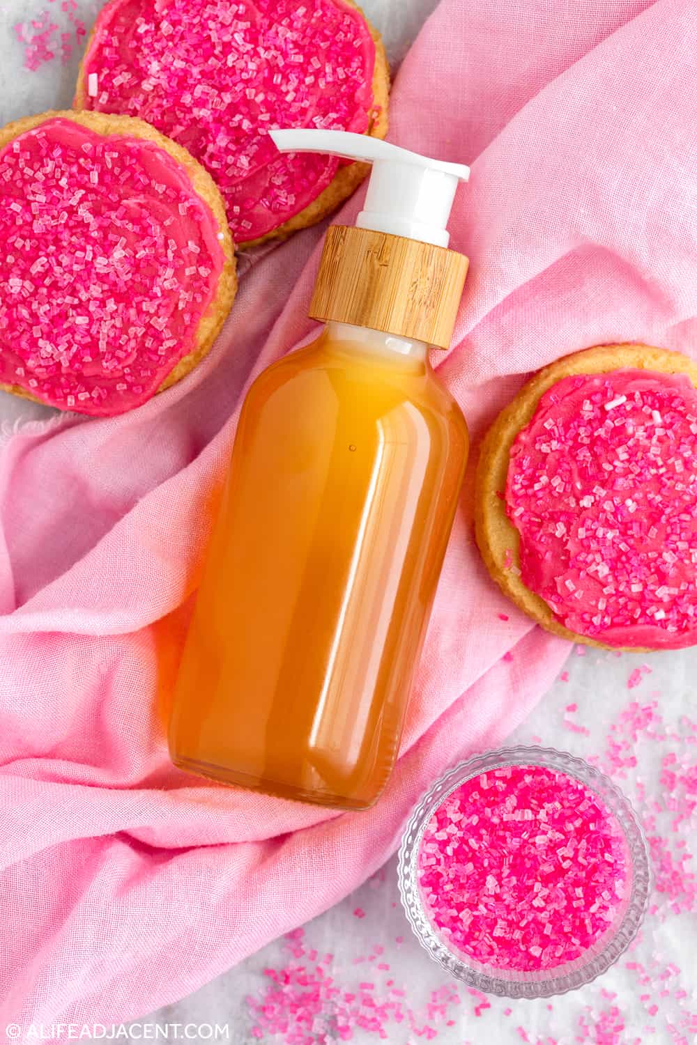 Natural sugar cookie perfume oil displayed on pink fabric with sugar cookies and pink sprinkles.