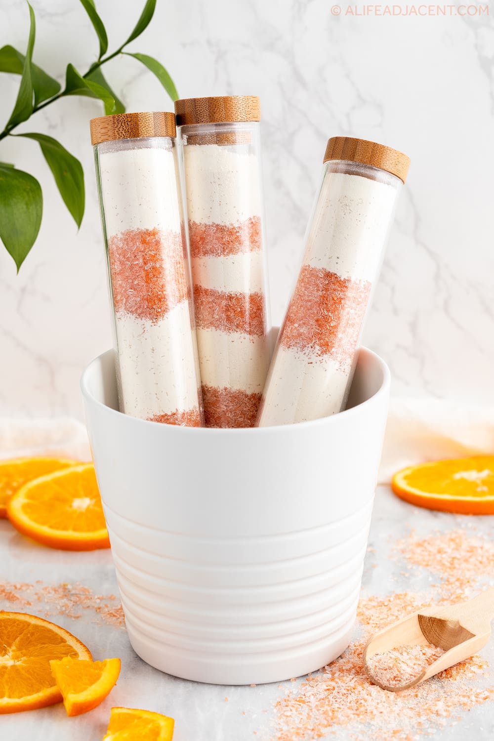 Homemade orange bath soak layered in bath salt tubes in decorative flower pot with orange slices