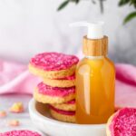 DIY body oil with natural sugar cookie fragrance displayed on a marble dish with frosted sugar cookies.
