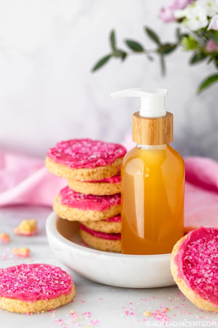 DIY body oil with natural sugar cookie fragrance displayed on a marble dish with frosted sugar cookies.