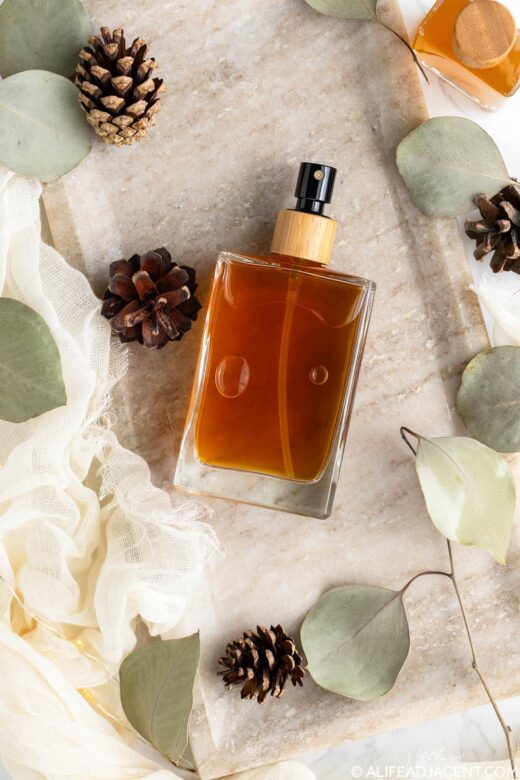 DIY body spray for men in a glass perfume bottle, displayed on a marble tray with eucalyptus leaves and pinecones.