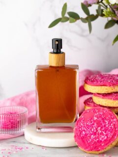 DIY sugar cookie body spray made with essential oils and natural perfumery oils, pictured beside a stack of pink frosted sugar cookies.