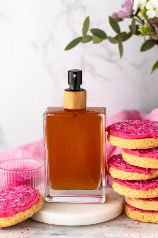 DIY sugar cookie perfume on a marble coaster, surrounded by pink sugar cookies.